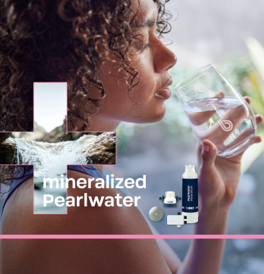 Frau trinkt aus einem Glas Wasser, daneben Produkte mit "mineralized Pearlwater".